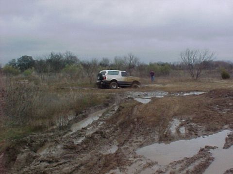 1990 Ford Bronco - A white 1990 Ford Bronco is stuck in a muddy field under an overcast sky.