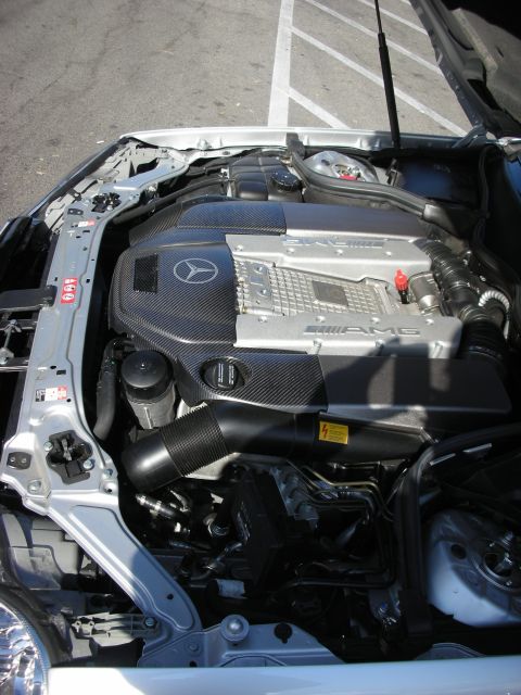 1998 Ford Crown Victoria - Engine bay of a Mercedes showing a supercharged AMG V8 with a carbon-fiber cover bearing the Mercedes star and AMG script.