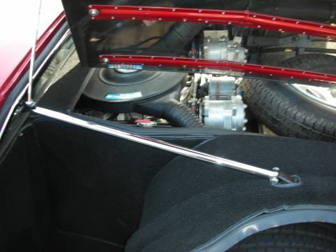 1998 Ford Crown Victoria - Detail of an engine compartment behind a red riveted trim panel, showing a chrome strut brace and spare tire.