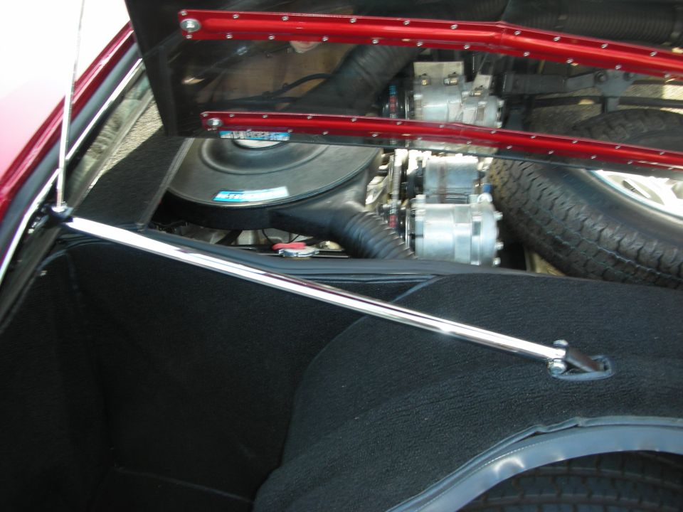 Engine compartment behind red trim panel with chrome strut brace and tires