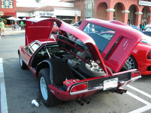 1998 Ford Crown Victoria - red mid-engine sports car displayed with its rear clamshell and doors open, showing the engine, at an outdoor car show.