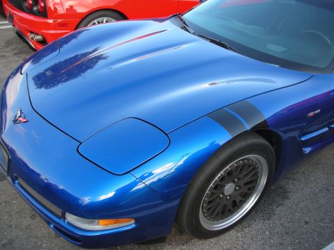 1998 Ford Crown Victoria - Front fender and fuel-door area of a blue Chevrolet Corvette with a black racing stripe and dark mesh wheels.