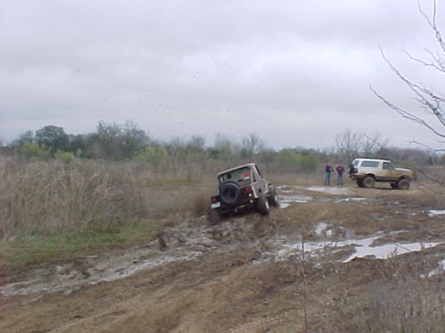 Two off-road vehicles navigating a muddy terrain under an overcast sky