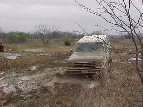 1990 Ford Bronco - A Ford Bronco navigates a muddy terrain under an overcast sky.