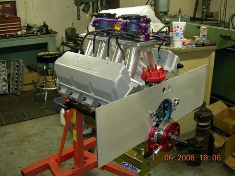 1972 Ford Ranchero - A silver engine with purple accents and dual carburetors is displayed on a red engine stand in a workshop.