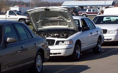 2000 Ford Crown Victoria - A white Ford Crown Victoria has its hood open, revealing the engine bay, with another similar car parked nearby.