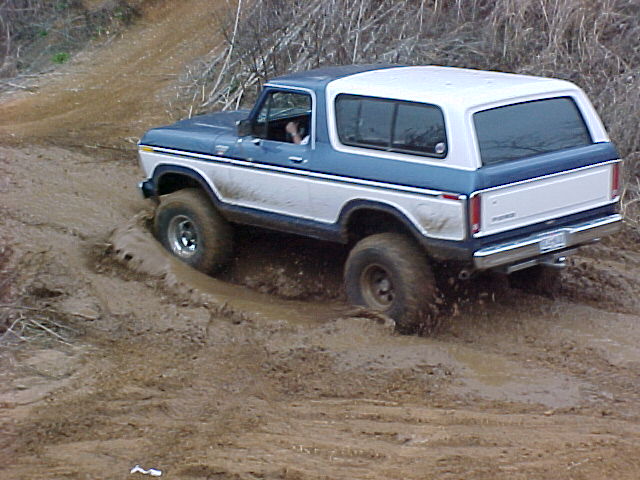 Blue and white late-70s full-size Bronco climbing a muddy off-road bank