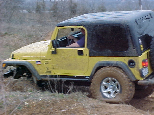 Yellow Jeep Wrangler with hardtop climbing a brushy off-road slope, driver inside