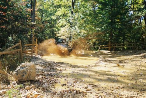 1993 Ford Bronco - An SUV navigates a muddy obstacle course, kicking up a large spray of water and dirt.