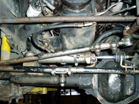 2000 Ford E350 - Close-up of the steering system components underneath a vehicle, showing various metal rods and hydraulic lines.