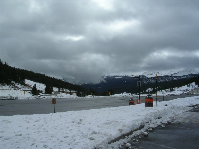 snowy mountain landscape with a parking lot and overcast sky. Supermotors.net logo in corner
