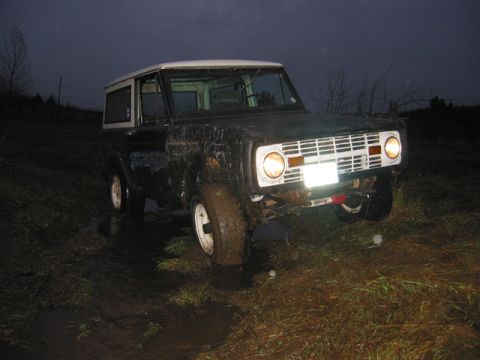 1968 Ford Bronco - This dark SUV with a white top appears to be stuck in muddy terrain at dusk.