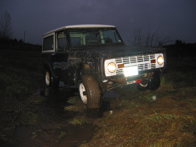 Front view of a dark SUV with a white top stuck in mud