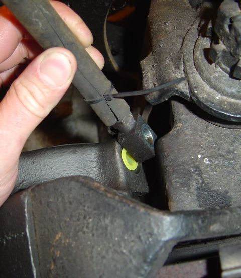 1986 Ford Bronco - A hand secures a brake hose with zip ties to a metal component, revealing a yellow insert within the connection.
