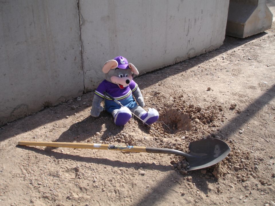 Chuck E. Cheese plush toy with shovel next to a hole