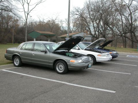2001 Ford Crown Victoria - Three Ford Crown Victorias parked in a lot with their hoods open.