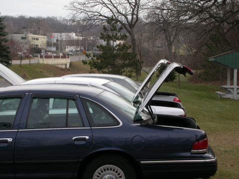 2001 Ford Crown Victoria - Several sedans are parked in a row with their trunks open, including a dark blue 2001 Ford Crown Victoria.