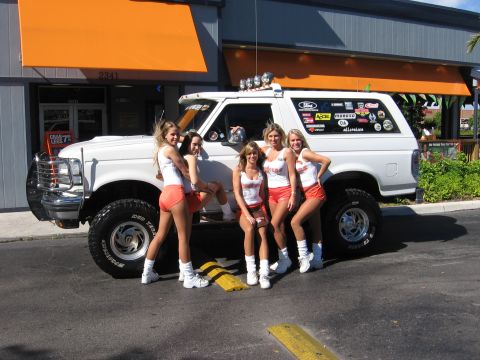 1995 Ford Bronco - White lifted Ford Bronco parked in front of a Hooters restaurant with five servers in uniform posing alongside it. The truck wears a chrome…