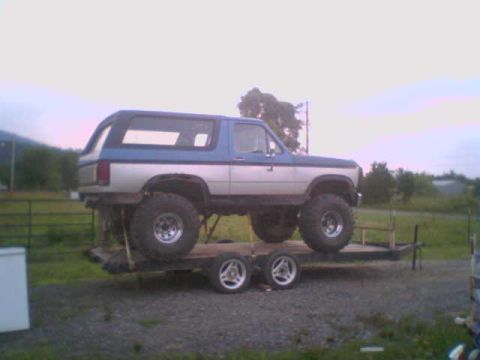 1985 Ford Bronco - A lifted Ford Bronco is transported on a trailer, its large tires and two-tone paint scheme visible.