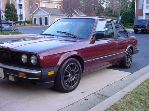 1984 BMW 3 Series - A maroon coupe is parked on a concrete surface with a black SUV in the background.