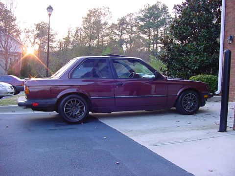 1984 BMW 3 Series - A maroon coupe with aftermarket wheels is parked outside. The sun is setting behind a street lamp.
