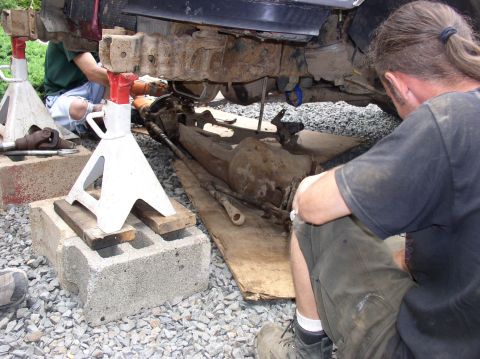 1996 Ford F-250 - Two people are working on the rusty undercarriage of a vehicle supported by jack stands.