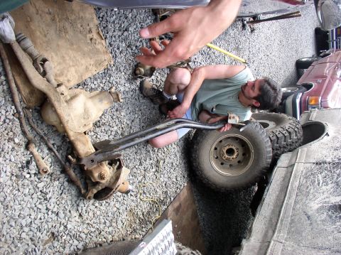 1996 Ford F-250 - A man is working on a vehicle's front axle assembly, with a maroon truck visible in the background.
