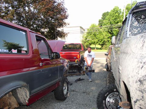 1996 Ford F-250 - Man works on trailer hitch between a red Ford Bronco and a muddy truck.