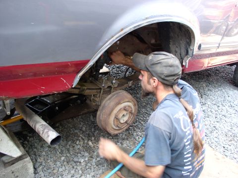 1996 Ford F-250 - A mechanic works on the rear suspension of a truck, with the wheel removed and the axle exposed.
