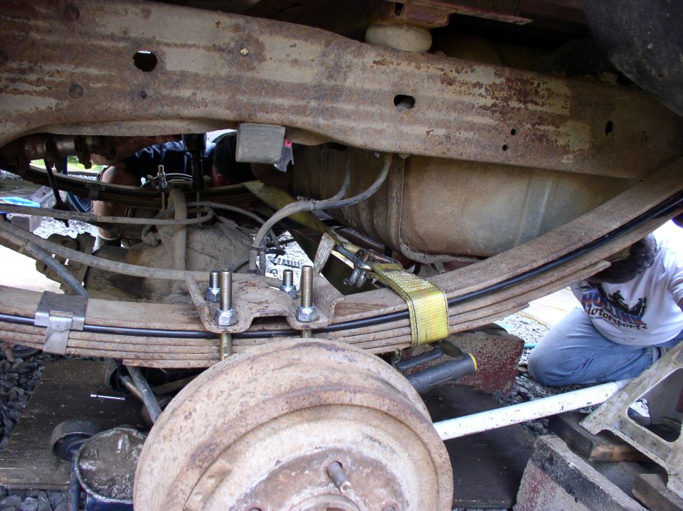 Undercarriage of a rusty truck with leaf springs and a fuel tank, showing a person working on it