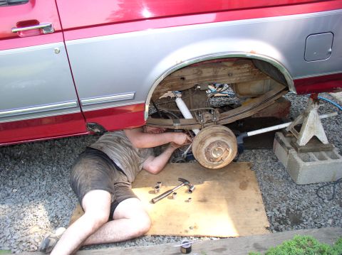 1996 Ford F-250 - Mechanic performs maintenance on the rear suspension of a red and silver pickup truck.