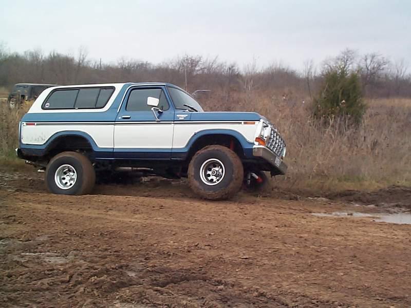 Blue and white lifted Ford Bronco parked in a brushy field, side profile