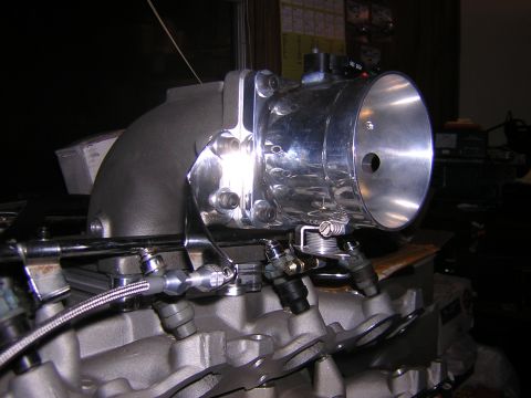 1979 Ford Bronco - A chrome throttle body is mounted on a grey engine manifold, showing fuel injectors and intake piping.