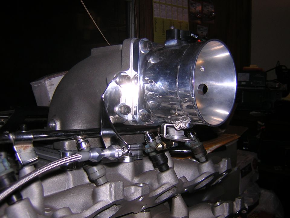 Close-up of a chrome throttle body attached to a grey engine manifold with fuel injectors