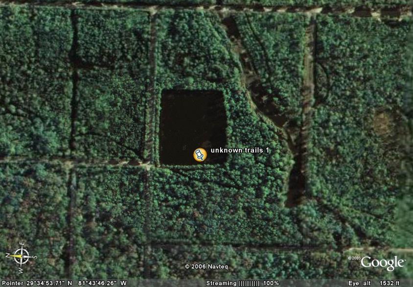 aerial shot of woods with a dark pond labeled 'unknown trails 1'