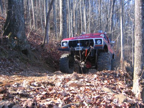1979 Ford Bronco - Modified 1979 Ford Bronco navigating a steep, leaf-covered trail in the woods.