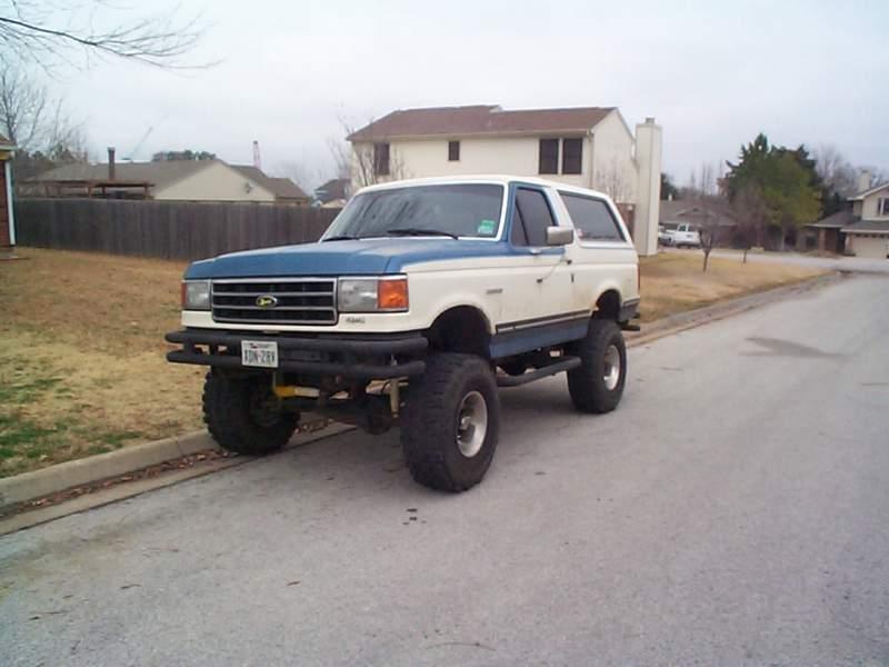 Blue and white lifted 1980s Ford Bronco parked on a suburban street, front quarter