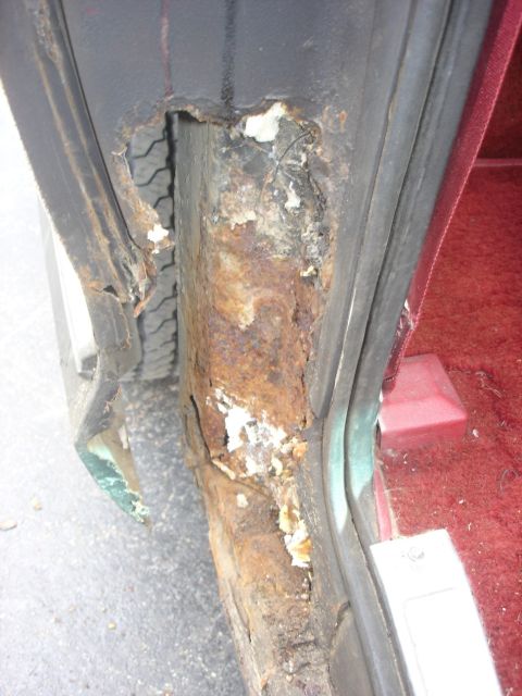 1979 Ford Bronco - Significant rust damage is visible on the vehicle's door frame, with a tire peeking through a hole.