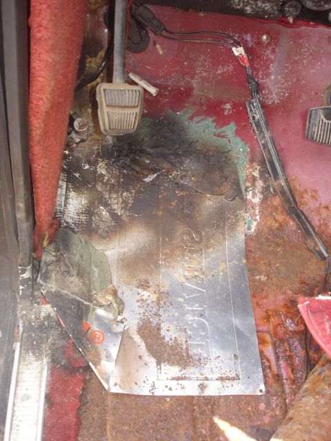 1979 Ford Bronco - The interior floor of a vehicle shows significant rust and damage, with pedals and wiring visible.