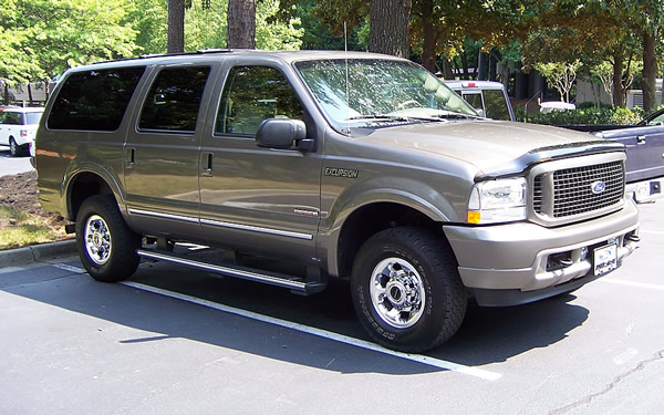 Tan Ford Excursion SUV, 3/4 front view, parked in a lot with trees