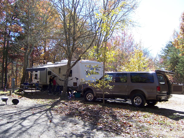 Tan Ford Excursion SUV towing a white travel trailer at a wooded campsite
