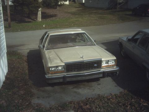 1985 Ford Crown Victoria LTD - A tan 1985 Ford Crown Victoria LTD is parked in a driveway next to another car.