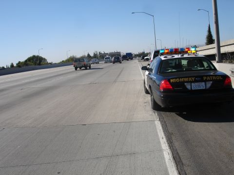 1993 Ford Taurus - A highway patrol car is stopped on the side of a busy freeway with other vehicles in motion.
