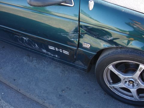 1993 Ford Taurus - Side view of a damaged green car door, showing dents and scratches, with a '24V DOHC' badge.