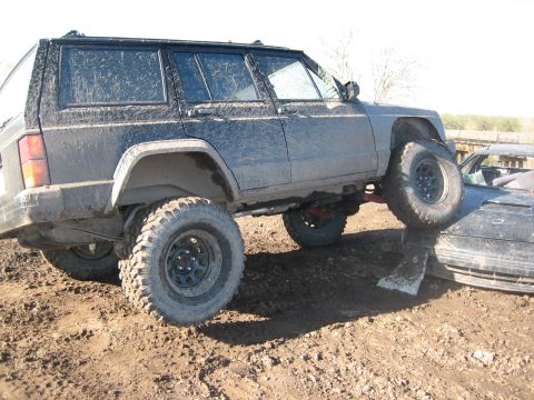 1995 Ford Bronco - Muddy Jeep Cherokee XJ is stuck, with its front tire resting on another vehicle.