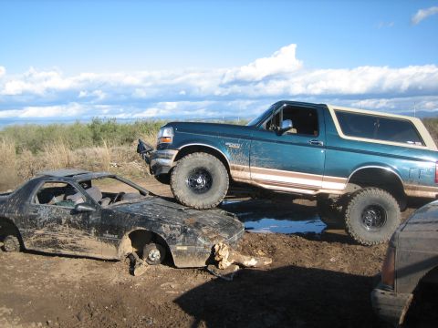 1995 Ford Bronco - Ford Bronco parked on top of a destroyed car in a muddy outdoor area.