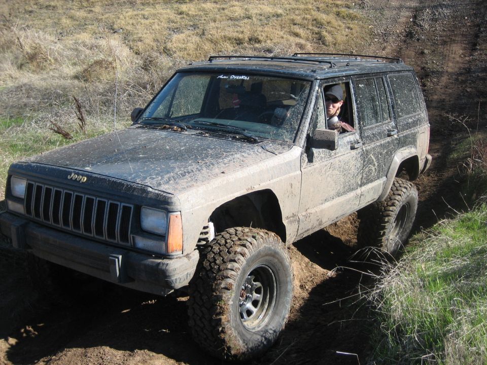 Mud-covered Jeep Cherokee XJ with off-road tires driving on a dirt trail