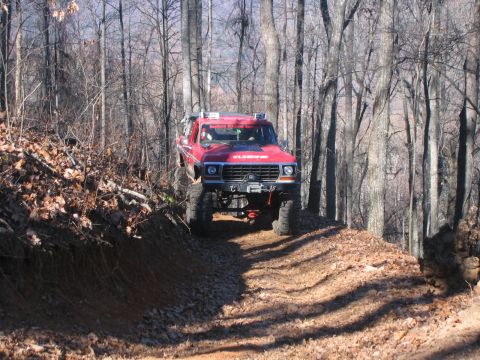 1979 Ford Bronco - A lifted red 1979 Ford Bronco navigates a wooded trail during an off-road excursion.