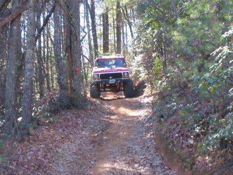 1979 Ford Bronco - A modified red SUV navigates a wooded trail with significant ground clearance.