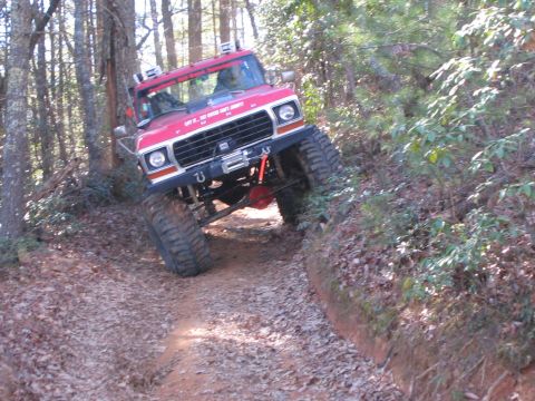 1979 Ford Bronco - A red 1979 Ford Bronco, modified for off-road use, climbs a steep, leaf-covered dirt path through a forest.